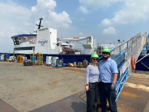 Emma and James stood in front of Menawethan at the Shipyard in Vietnam