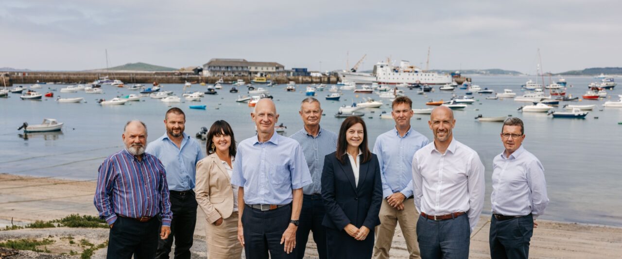 Isles od Scilly Steamship Group - Board of Directors stood in front of Town Beach, St Mary's, Isles of Scilly with St Mary's Harbour in the background, with Scillonian III berthed.